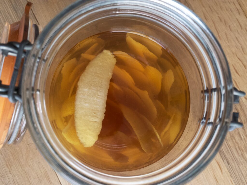 Lemon peel for limoncello sitting in mason jar filled with vodka that has been infused with the lemon for three weeks