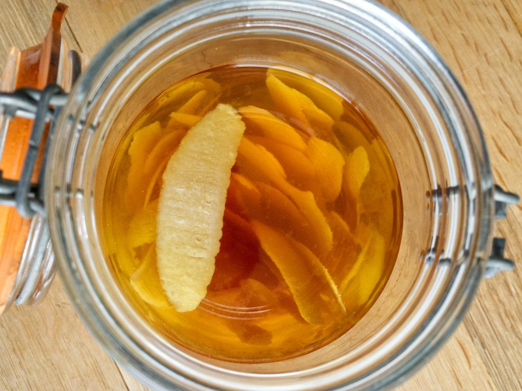 Lemon peel for limoncello sitting in mason jar filled with vodka that has been infused with the lemon for three weeks