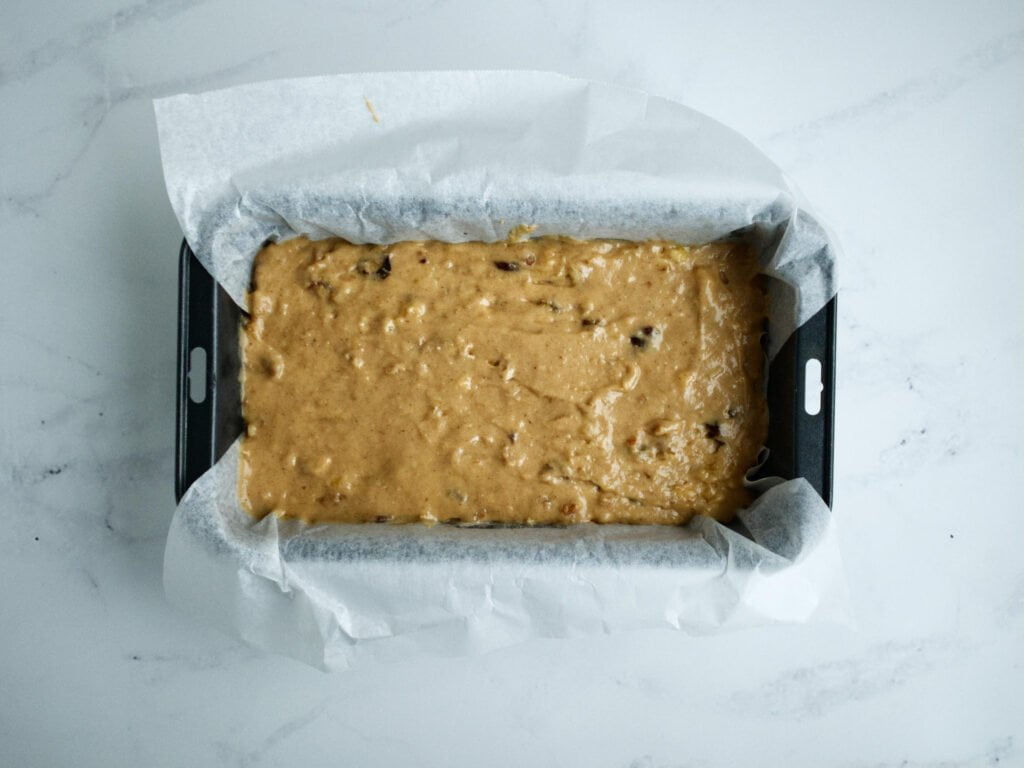 Banana bread mixture in loaf pan lined with baking paper
