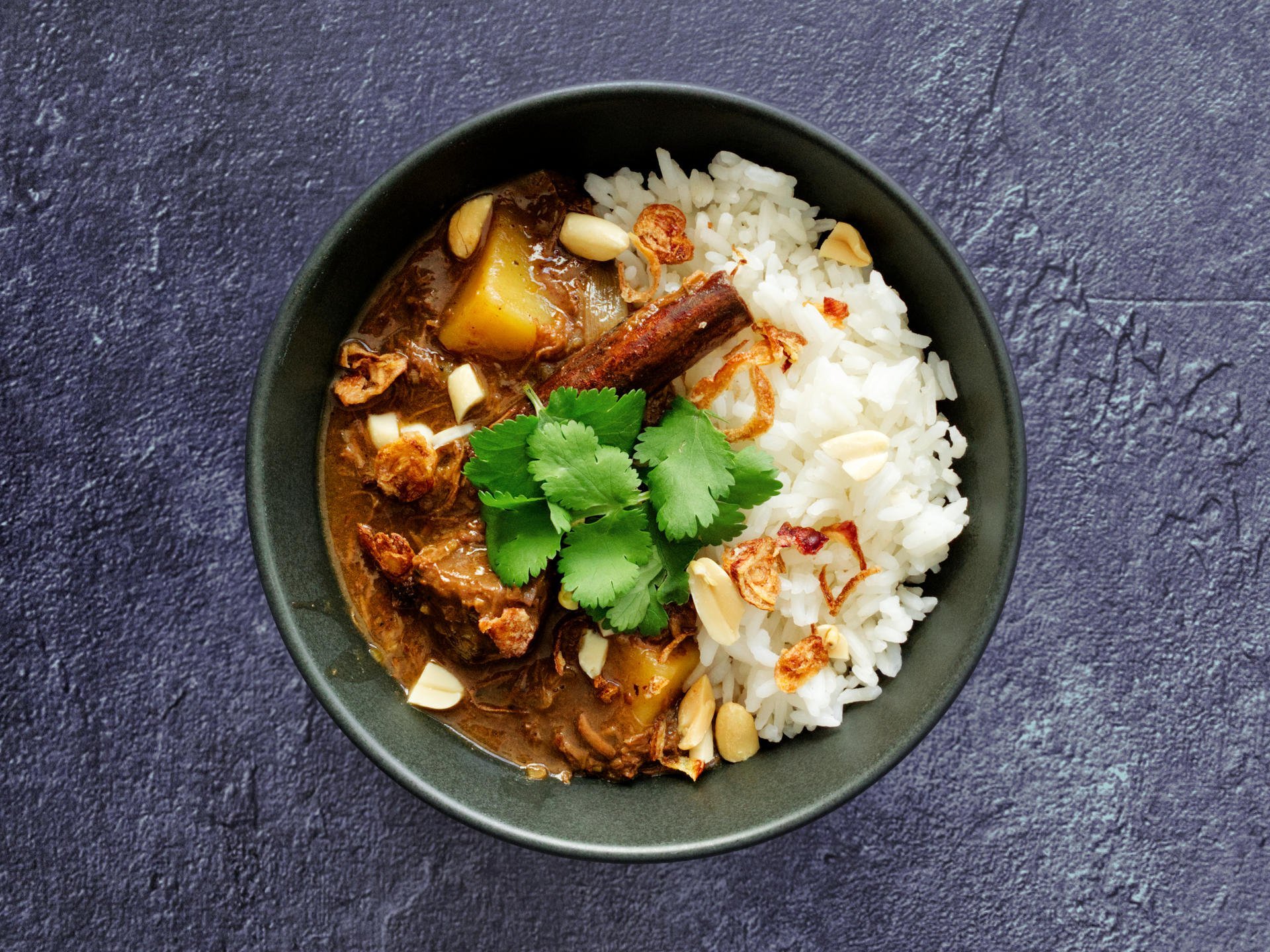 Beef massaman curry served in a bowl with rice and garnished with coriander, peanuts and dried shallots