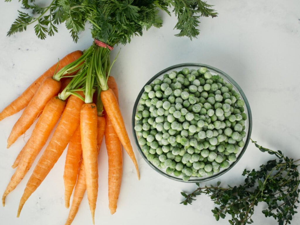 A bunch of Dutch carrots, bowl of frozen peas and sprigs of fresh thyme