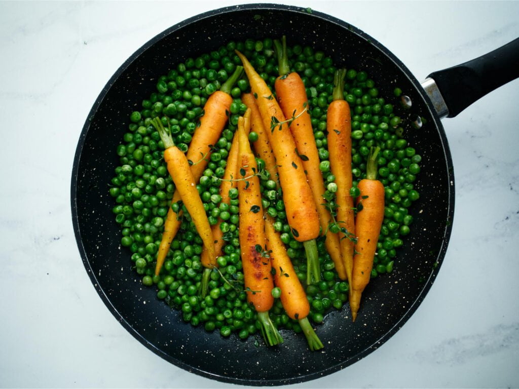 Frying pan containing braised Dutch carrots and baby peas
