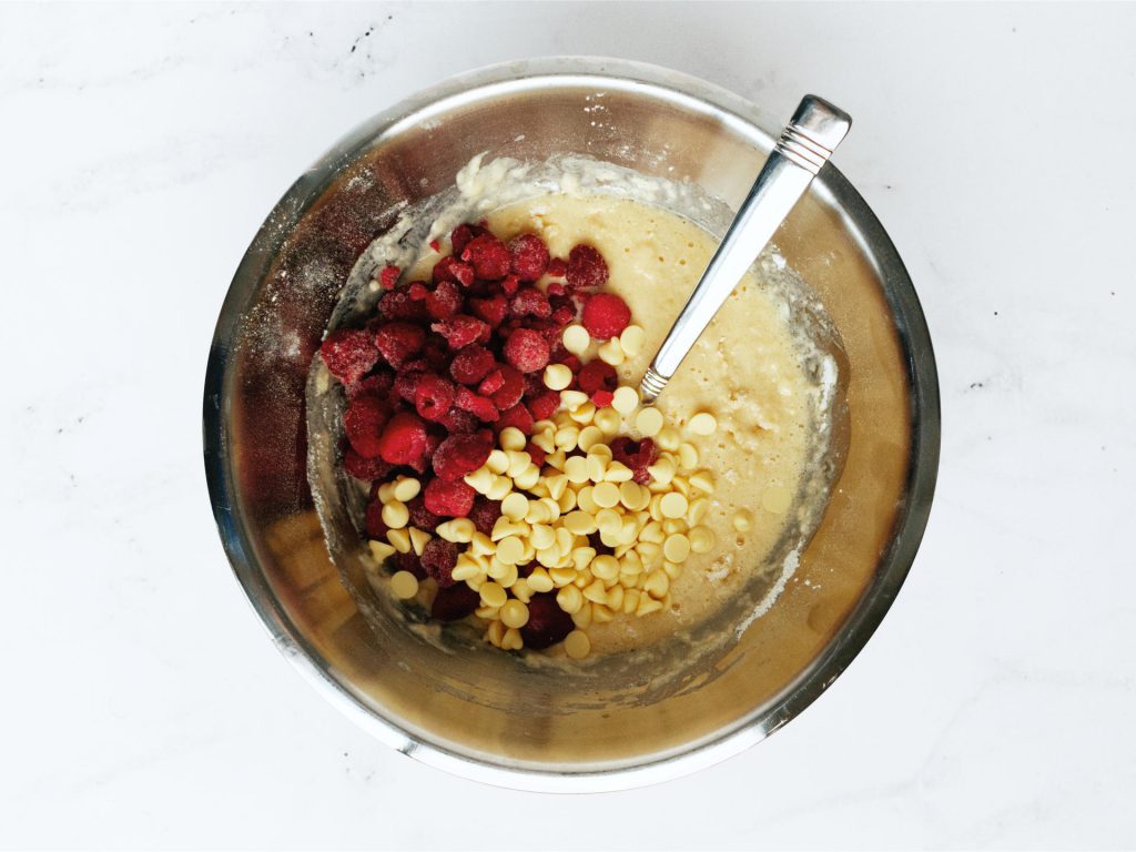 Mixing bowl containing the ingredients mix with raspberries and white chocolate on top