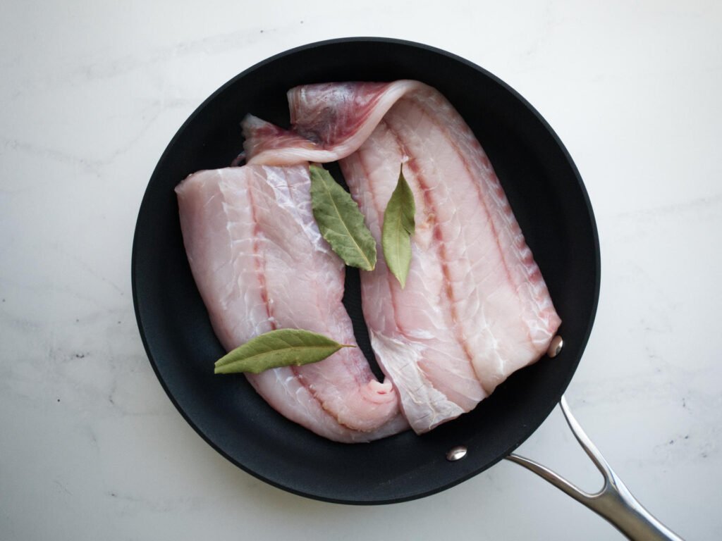 Raw Rockling fillets and sage leaves in a frying pan
