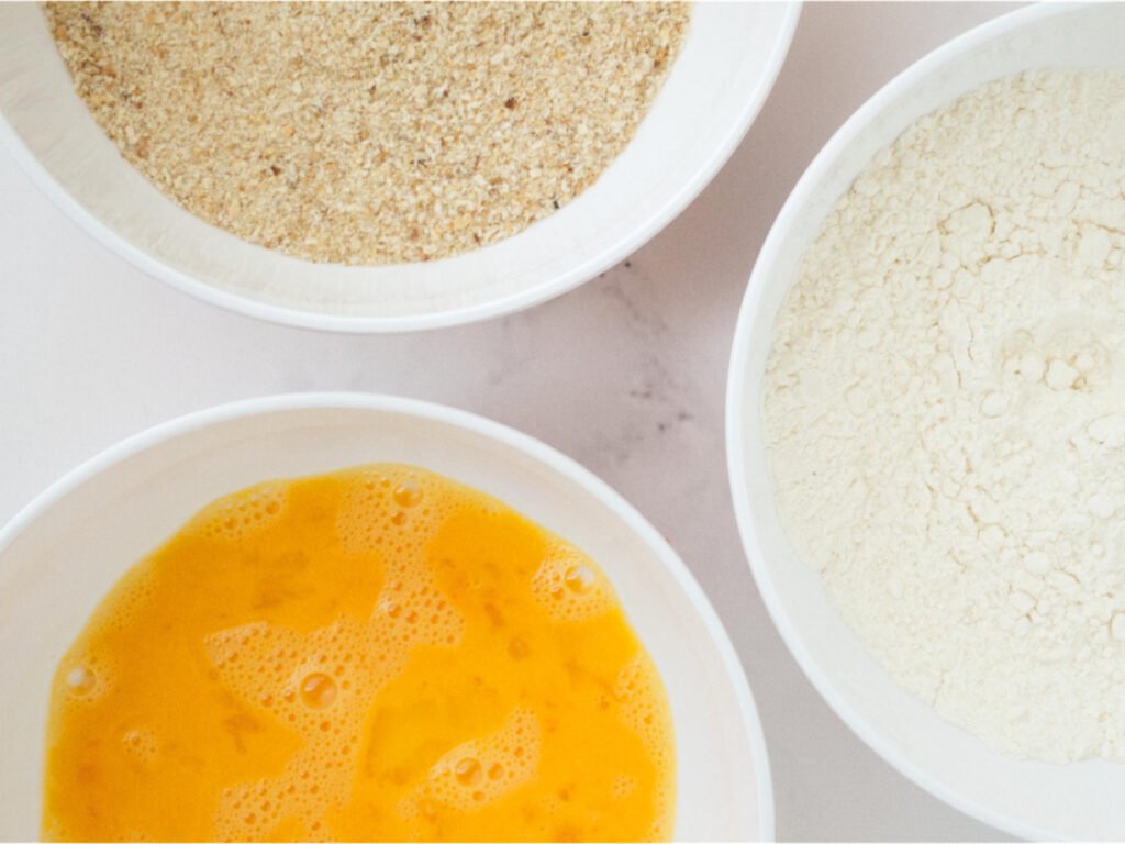 Three bowls containing crumbing ingredients - one each of flour, egg and breadcrumbs