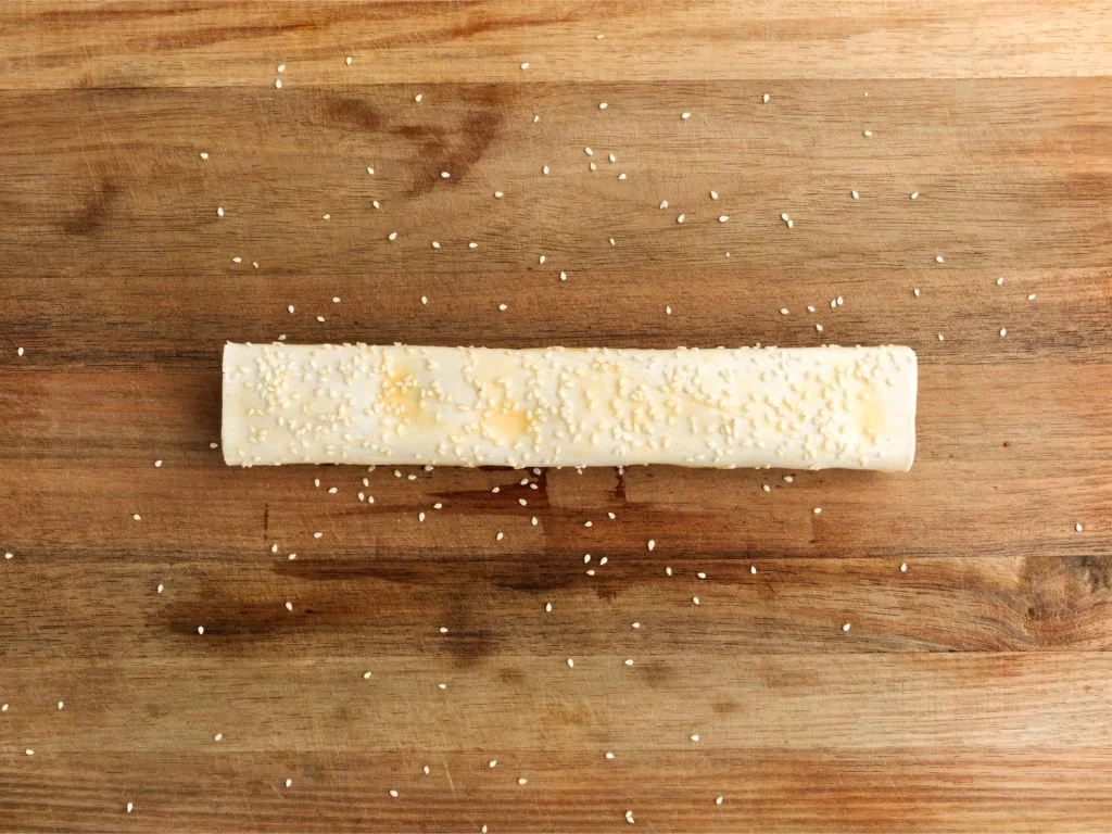 Egg washed sausage roll covered with sprinkling of sesame seeds