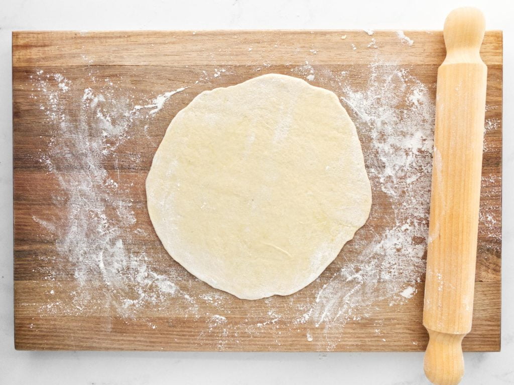 Rolled out flatbread dough on a wooden kitchen board.
