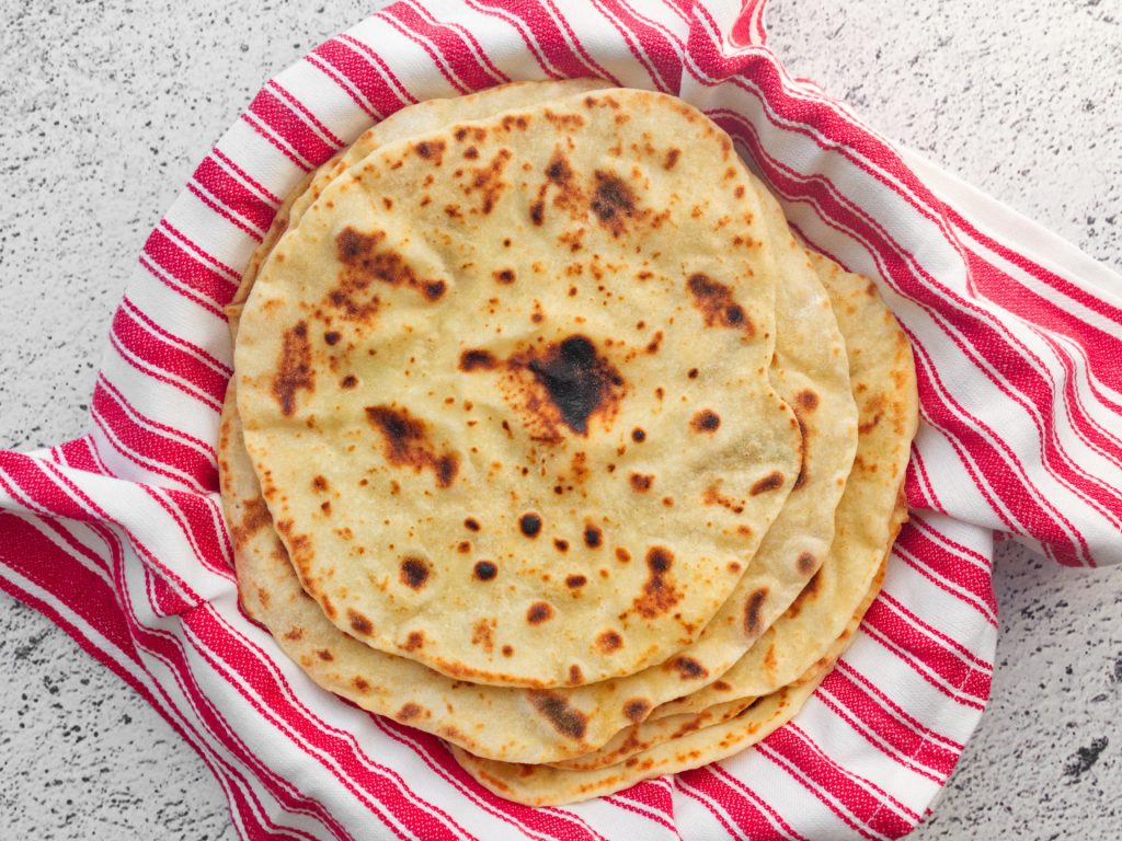 Stack of cooked flatbreads wrapped in tea towel.